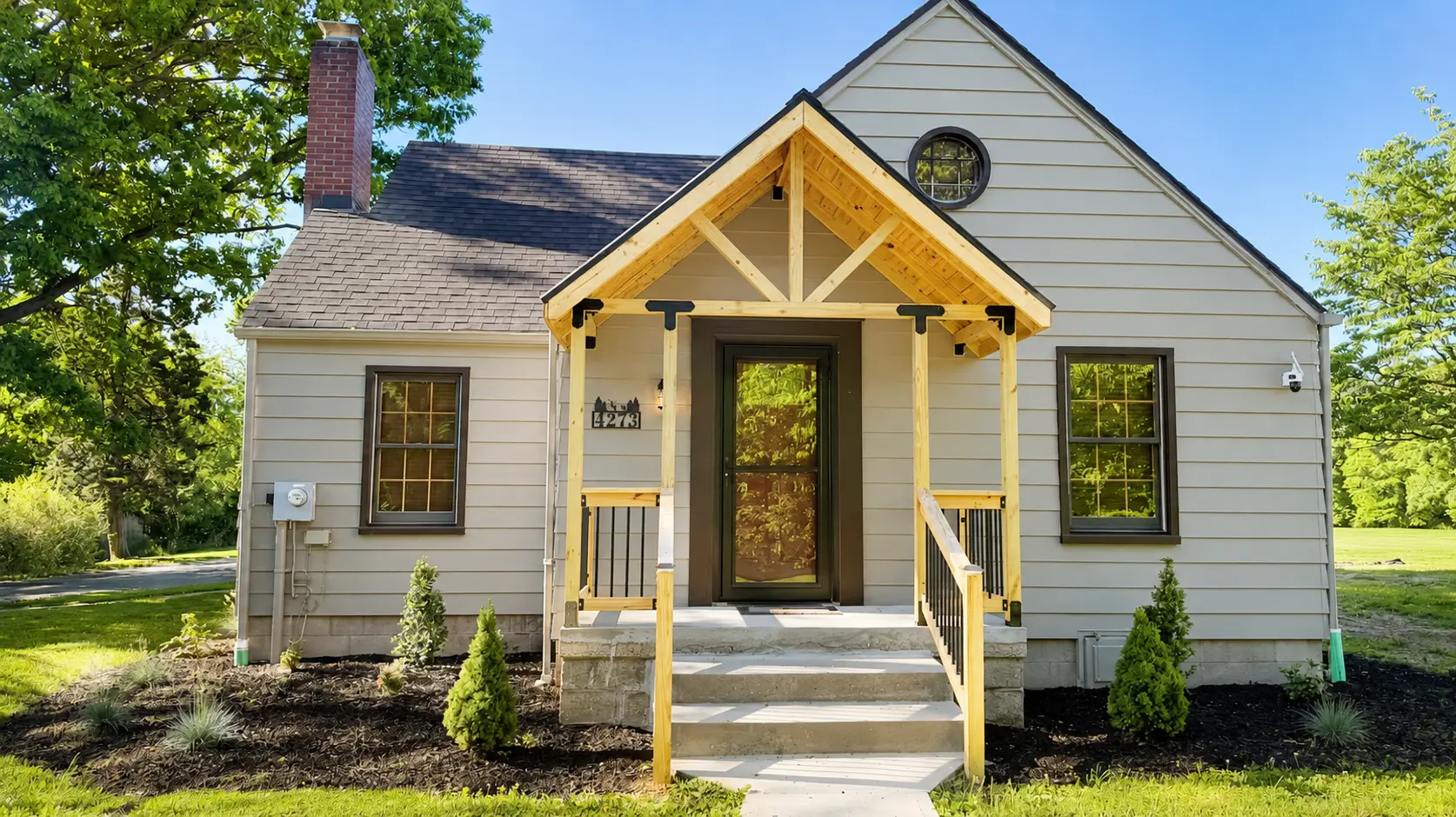 Front exterior of the country home with a wood porch, gabled roof and green lawn on a sunny day
