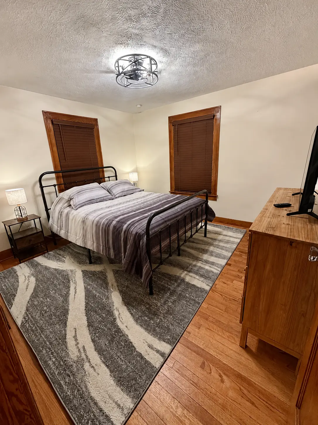 Main floor bedroom seen from the doorway with a queen bed, nightstands and area rug